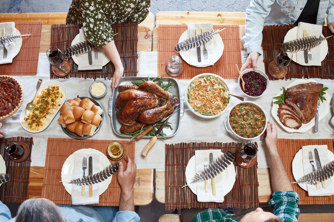 Overhead photo of a family and friends seated at a Thanksgiving table sharing dishes of food and eating.