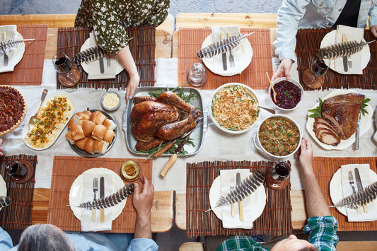 Overhead photo of a family and friends seated at a Thanksgiving table sharing dishes of food and eating.