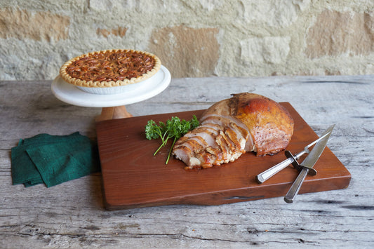 Sliced mesquite turkey on a serving platter with a pecan pie in the background.