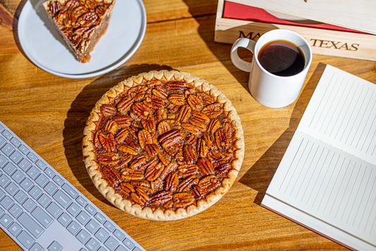 Fresh pecan pie lying next to a keyboard, with a slice of pie sitting on a white plate.