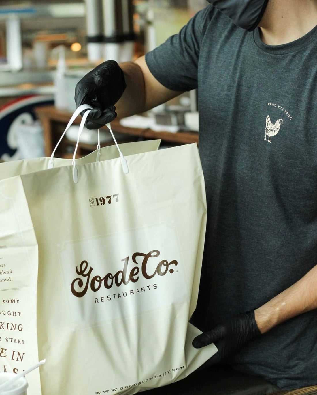 Close-up photo of a Goode Co. takeout bag being handed over by an employee to a customer.